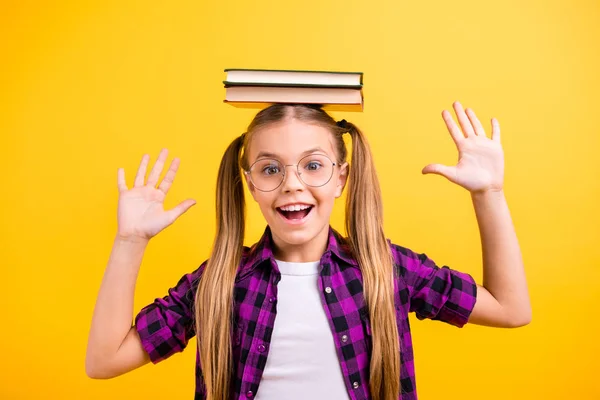 Nahaufnahme Foto der kleinen Schülerin halten Buch auf dem Kopf lachend heben Arme Luft tragen Spezifikationen kariertes Hemd isoliert gelb Hintergrund — Stockfoto