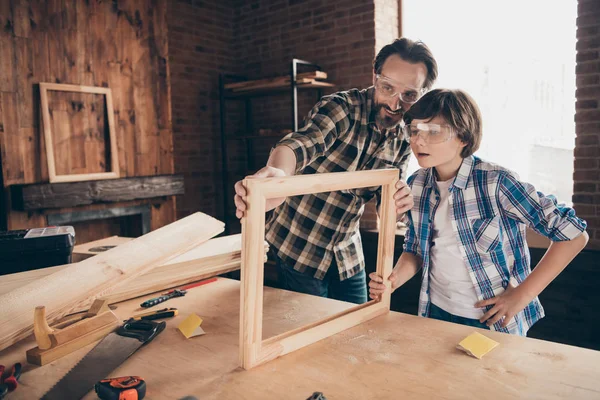 Portrait inspired child boy positive cheerful daddy craftsmen occupation workstation masterclass hardwood desktop desk touch wood hone indoors bearded checkered shirt fix glasses goggles protective