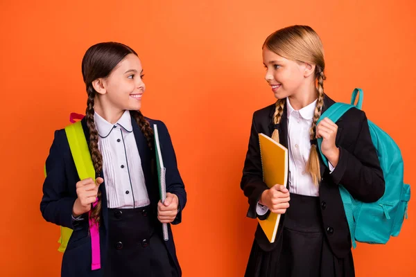 Közelről fotó két szép lány a kis női vicces karok tervezők kész az első tanulni nap mondani nyaralás Hírek kopás fejrevalók ing blézer iskola formájában táska elszigetelt élénk narancssárga háttér — Stock Fotó