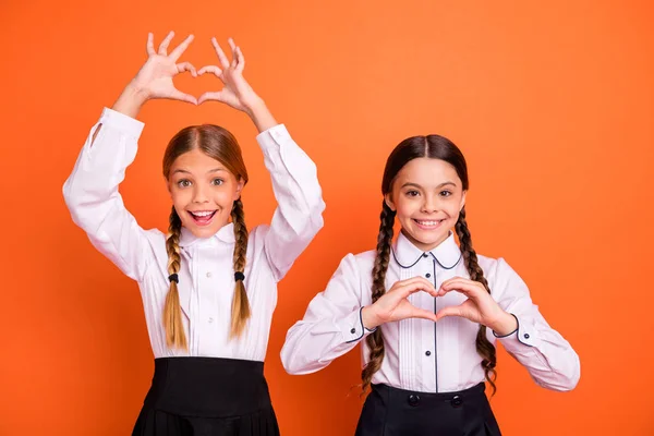 Porträt von zwei Personen schön attraktiv charmant niedlich fröhlich fröhlich liebenswert lustig Pre-Teen Mädchen zeigen Herzform isoliert über hellen lebendigen Glanz orange Hintergrund — Stockfoto