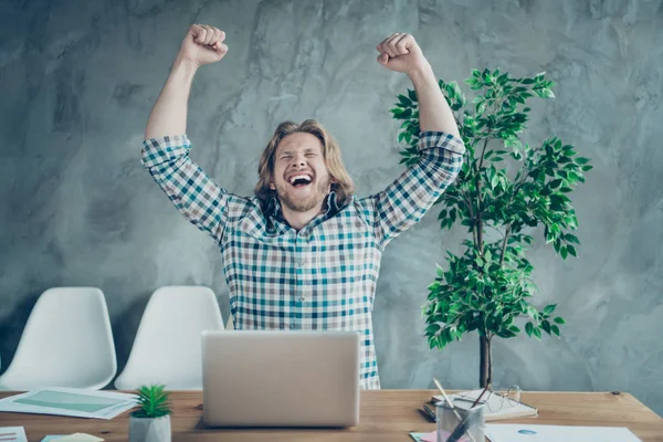 Porträt einer fröhlichen Freelancerin mit blonden Haaren, die schreiend die Fäuste hebt und im karierten karierten Hemd im Industriepark sitzt — Stockfoto