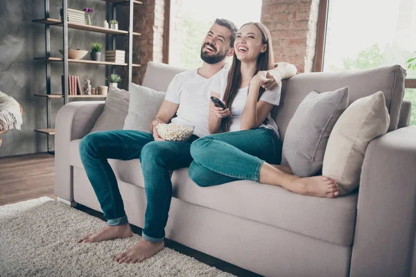 Удивительная пара держит тарелку с попкорном смотреть любимое юмористическое шоу сидя диван в помещении — стоковое фото