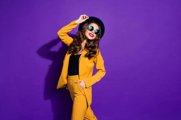 Фото модної леді, що йде по вулиці носити стильний капелюх жовтий костюм ізольований фіолетовий фон — стокове фото