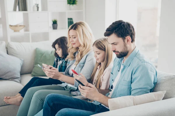Familia joven dos niños adoptados acogedor sofá sentado mira teléfonos no se preocupan concepto de adicción —  Fotos de Stock