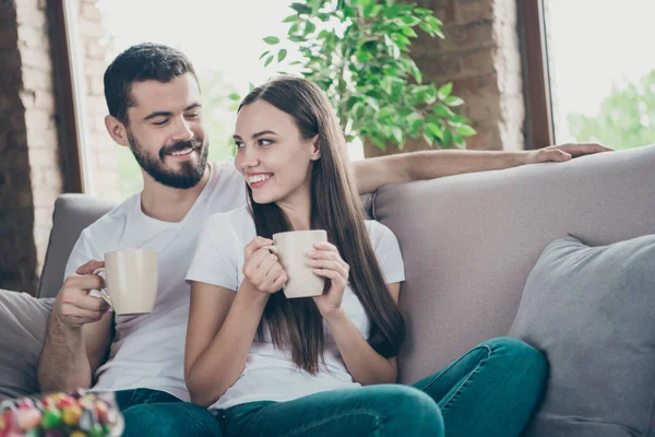 Foto de casal adorável no amor segurando as mãos de bebidas quentes comunicando sentado sofá acolhedor dentro de casa — Fotografia de Stock