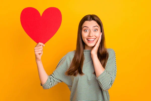 Foto de linda menina legal regozijando-se sobre ter sido dotado de grande coração vermelho para o dia dos namorados, enquanto isolado com fundo amarelo — Fotografia de Stock