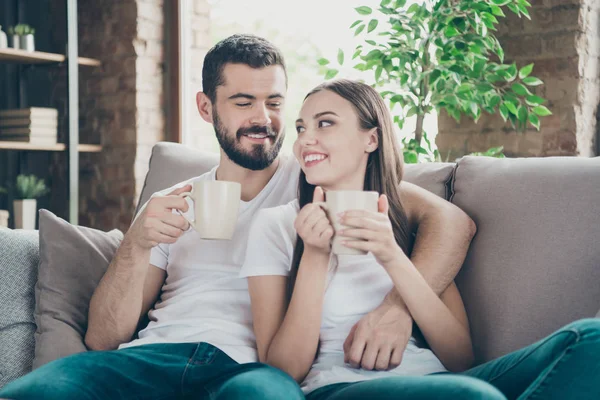 Foto de casal adorável no amor segurando as mãos de bebidas quentes comunicando sentado sofá acolhedor dentro de casa — Fotografia de Stock