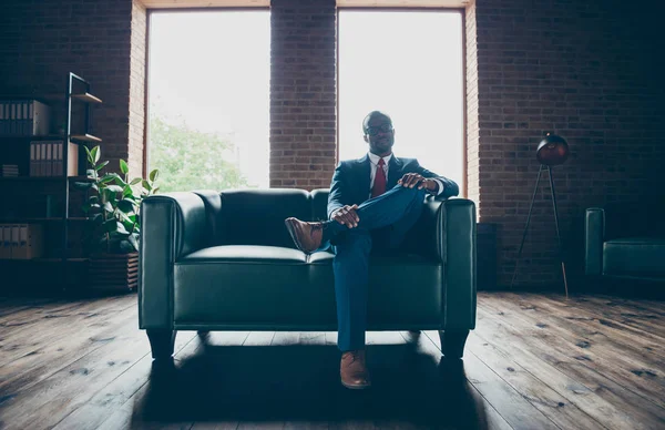 Foto de chico macho de piel oscura sentado sofá de oficina usar especificaciones y traje corporativo — Foto de Stock