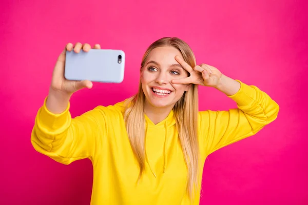 Foto de señora bonita haciendo selfies mostrando v-signo cerca del ojo desgaste sudadera con capucha amarilla aislado fondo rosa —  Fotos de Stock