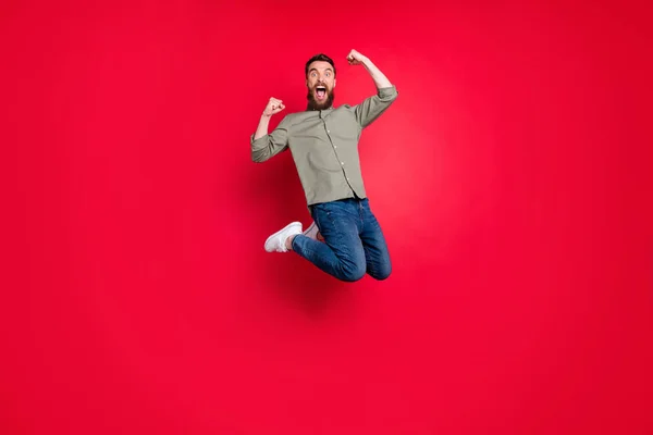 Foto de cuerpo entero del hombre alegre alegre loco que usa la ropa vaquera de los pantalones vaqueros que salta con felicidad mientras que está aislado con el fondo rojo — Foto de Stock