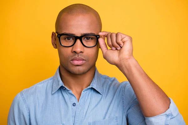 Foto de primer plano de piel oscura macho atento que mira las especificaciones de toque de la mano usan jeans camisa de mezclilla aislado fondo amarillo brillante —  Fotos de Stock