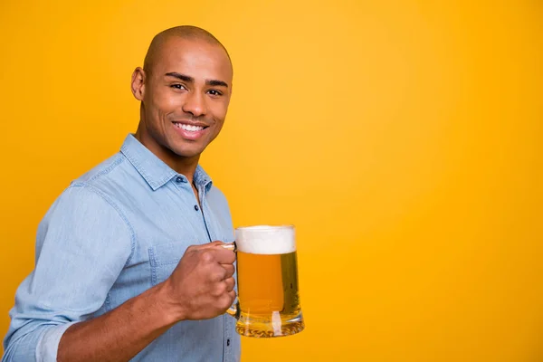 Foto de piel oscura fresco increíble chico toma de las manos vaso de cerveza permite celebrar el desgaste de la cara vaqueros camisa de mezclilla aislado fondo amarillo — Foto de Stock