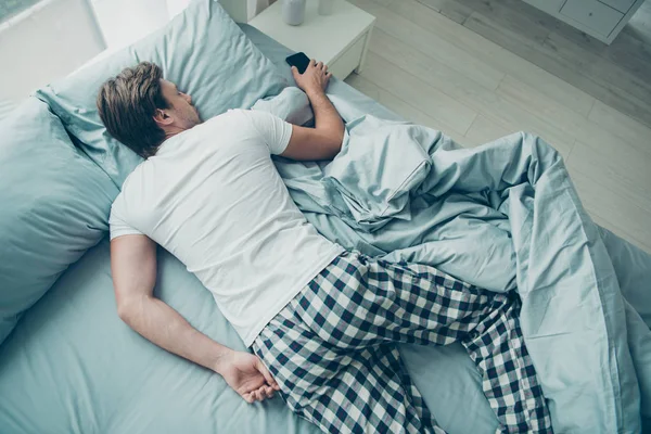 Top foto ad alto angolo di gioventù pacifica sdraiata sul letto con smart phone indossando t-shirt bianca a scacchi pantaloncini a quadri in camera all'interno — Foto Stock