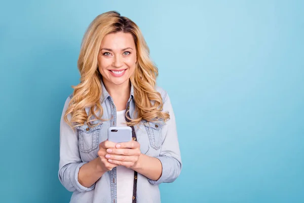 Portrait of cheerful charming lady with toothy smile holding modern technology looking at camera isolated over blue background — Stock Photo, Image