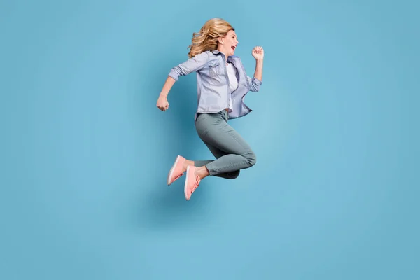 Mavi arka plan üzerinde izole pantolon giyen hareketli çalışan bağıran neşeli bayan tam boy profil yan fotoğraf — Stok fotoğraf