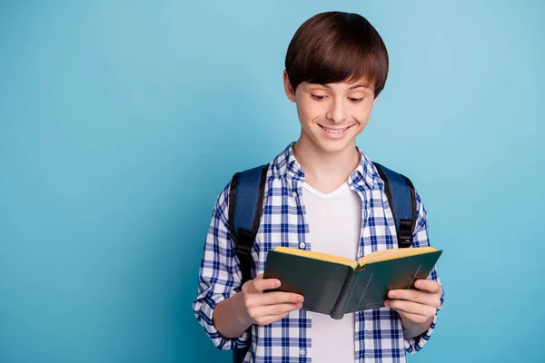 青い背景の上に隔離されたチェックのチェックのチェックのシャツを着て印刷された教科書を持つかわいい少年の肖像画 — ストック写真