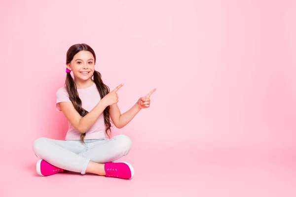 Volledige lichaam foto van koele kleine dame zittend vloer geven vingers lege ruimte gekleed casual outfit geïsoleerd roze achtergrond — Stockfoto