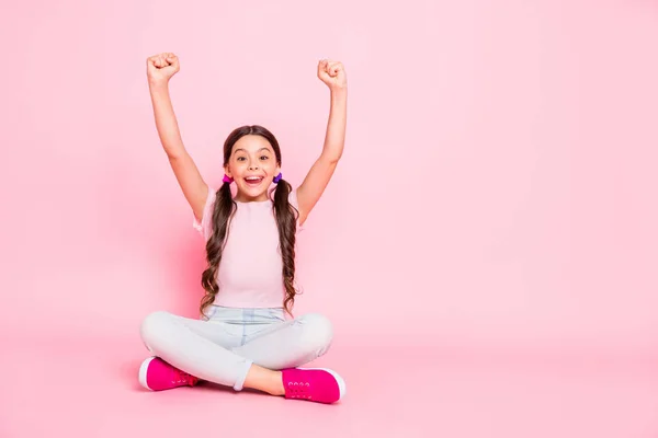 Portret van verrukt kind raise vuisten schreeuwen schreeuwen ja zittend gekleed witte broek broek geïsoleerd over roze achtergrond — Stockfoto