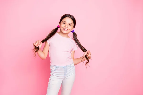 Retrato de niño bonito tocando coletas de pie mirando usando pantalones camiseta blanca aislada sobre fondo rosa — Foto de Stock