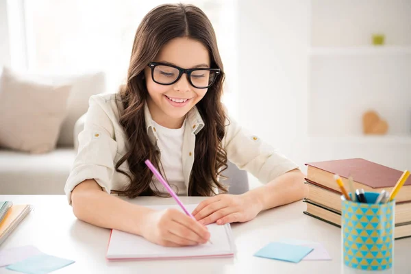 Close-up portrait of her she nice attractive charming cute cheerful cheery intellectual wavy-haired pre-teen girl wearing eyewear eyeglasses writing class work in light white interior room indoors — Stock Photo, Image