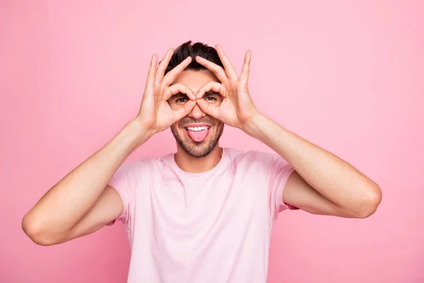 Increíble chico con símbolo okey cerca de los ojos fingir usar especificaciones pegando lengua traje casual aislado sobre fondo rosa — Foto de Stock