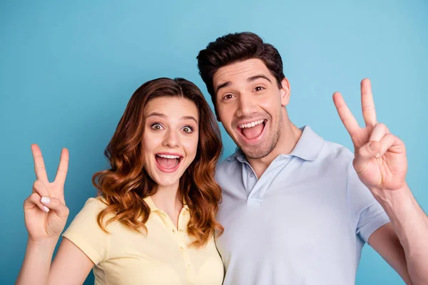 Foto de par engraçado animado v-sinal símbolo mãos positivo alegre dizer oi amigos usam t-shirts casuais isolado fundo azul — Fotografia de Stock