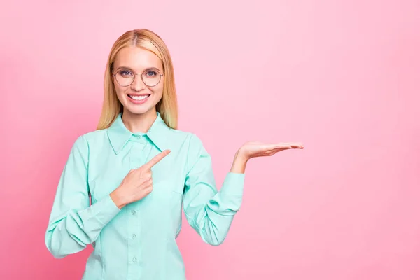 Ritratto di bella signora che mostra annunci puntando sorridente indossare occhiali occhiali camicia turchese isolato su sfondo rosa — Foto Stock