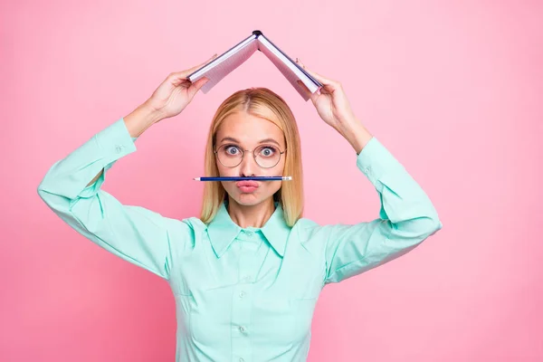 Porträtt av söt barnslig Lady håller hennes bok ovanför huvudet bär glasögon glasögon Teal skjorta isolerad över rosa bakgrund — Stockfoto