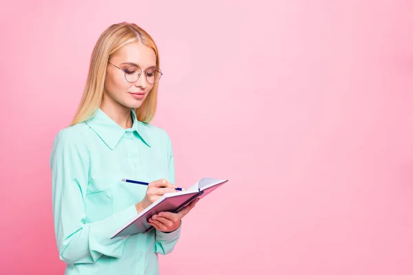 Foto girata di persona concentrata che scrive nel suo taccuino indossando camicia turchese verde acqua isolata su sfondo rosa — Foto Stock