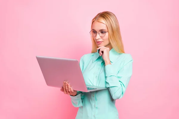 Portret van geconcentreerde meisje met brillen brillen houden gadget aanraken haar kin dragen Teal Turquoise shirt geïsoleerd over roze achtergrond — Stockfoto