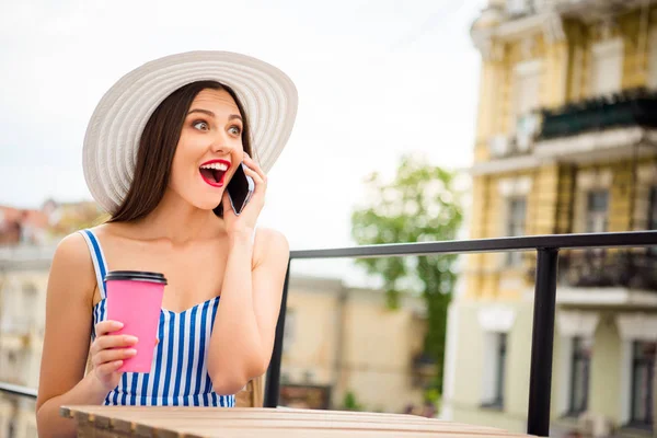 Bella dama hablando por teléfono escuchar grandes noticias sentado en acogedora cafetería calle usar sombrero de sol y vestido a rayas —  Fotos de Stock