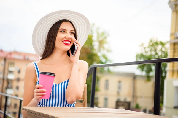 Bonita dama hablando por teléfono sentado acogedor en la calle café usar sombrero de sol y vestido a rayas —  Fotos de Stock