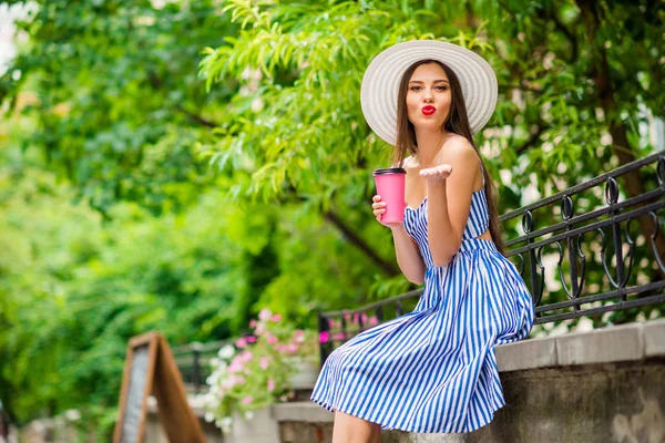 Удивительная леди отправляет бойфренда воздушный поцелуй благодарен за вкусный кофе идти носить солнцезащитную шляпу и полосатое платье — стоковое фото