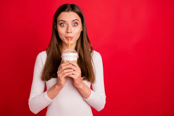 Φωτογραφία του ξαφνιασμένος κορίτσι έκπληκτος με τη γεύση του καφέ που ρουφάει με άχυρο, ενώ απομονωμένη με κόκκινο φόντο — Φωτογραφία Αρχείου