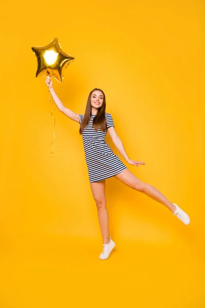 Függőleges fotó szép lány játszani nagy csillag alakú Légballon viselni csíkos fehér kék ruha elszigetelt sárga háttér — Stock Fotó