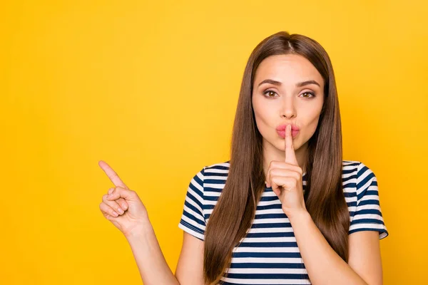 Foto de la señora divertida que indica el espacio vacío del dedo pidiendo mantener las noticias en secreto desgaste a rayas camiseta aislado fondo amarillo —  Fotos de Stock