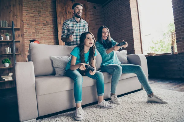 Retrato de personas emocionadas y niña con pelo moreno jugar videojuego con vaqueros jeans camiseta sentarse diván en casa en el interior — Foto de Stock