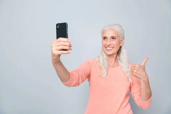 Закройте фотографию веселой уверенной в себе возбужденной мечтательной с волнистыми волосами старушки, делающей автопортрет на сером фоне — стоковое фото