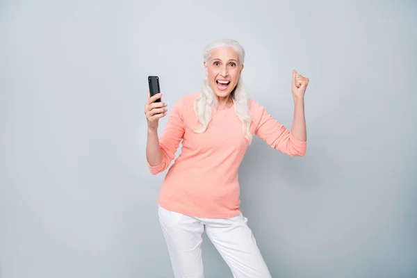 Фото современной прохладной восхитительной приятно приятно приятно оптимистичный милая старушка поднимает кулак вверх с помощью телефона изолированный серый фон — стоковое фото