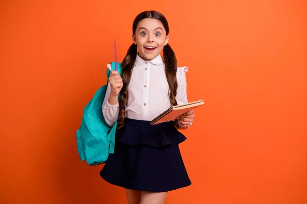 Retrato surpreendido criança surpreso segurar mão homework pensamentos imprssed inteligente moderno elegante cauda rabo de cavalo pigtails vestido branco camisa blusa moderna isolado mochila de fundo laranja — Fotografia de Stock