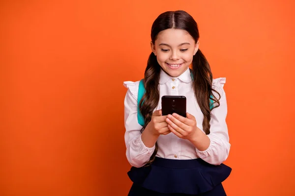 Retrato de adorable niño concentrado mantenga la mano dispositivo comunicación blogging desgaste falda vestido blanco moderno colas blusa camisa elegante moda aislado fondo naranja — Foto de Stock