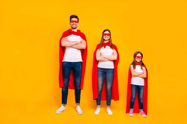 Três membros da família jogando desenhos animados personagens incríveis usam capas de super-herói isolado fundo amarelo — Fotografia de Stock