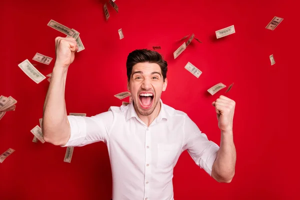 Fotografie úspěšného vítězného vítěze, který stojí v dešti bankovek z měnových peněz, zatímco je izolovaný s červeným pozadím — Stock fotografie