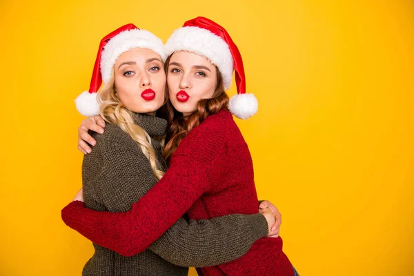 Pretty two ladies sending boyfriends air kisses wear knitted jumpers and santa hats isolated yellow background — Stock Photo, Image