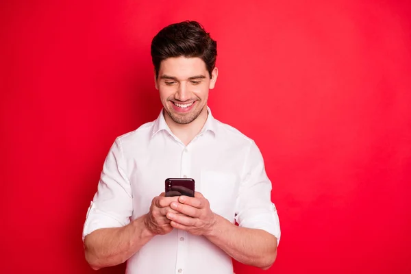 Foto de dente sorrindo homem moderno digitando mensagem para alguém com seu telefone enquanto isolado com fundo vermelho — Fotografia de Stock