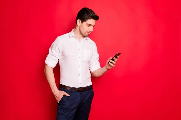 빨간 배경으로 고립 된 동안 흥미로운 무언가를 찾아 전화를 응시하는 매력적인 남자의 사진 — 스톡 사진