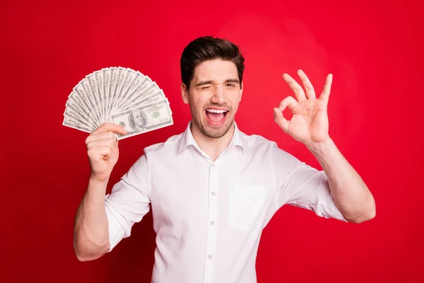 Foto de blanco guapo parpadeando hombre rico guiño que muestra que todo está bien mientras está aislado con fondo rojo — Foto de Stock