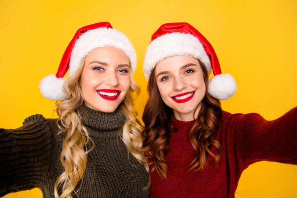 Pretty two ladies making festive self photos wear knitted jumpers and santa hats isolated yellow background — Stock Photo, Image