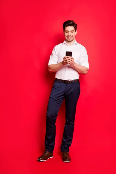 Vertikal full längd kroppsstorlek foto av stilig man tittar på något roligt på sin telefon medan isolerade med röd bakgrund — Stockfoto