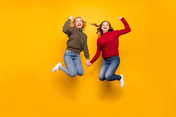 Foto de longitud completa de señoras lindas saltando alto celebrando ganar desgaste suéteres de punto aislado fondo amarillo — Foto de Stock